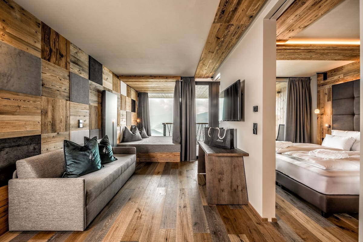 A modern hotel room with a wooden wall panel, a sofa, a bed, and a desk with a chair.
