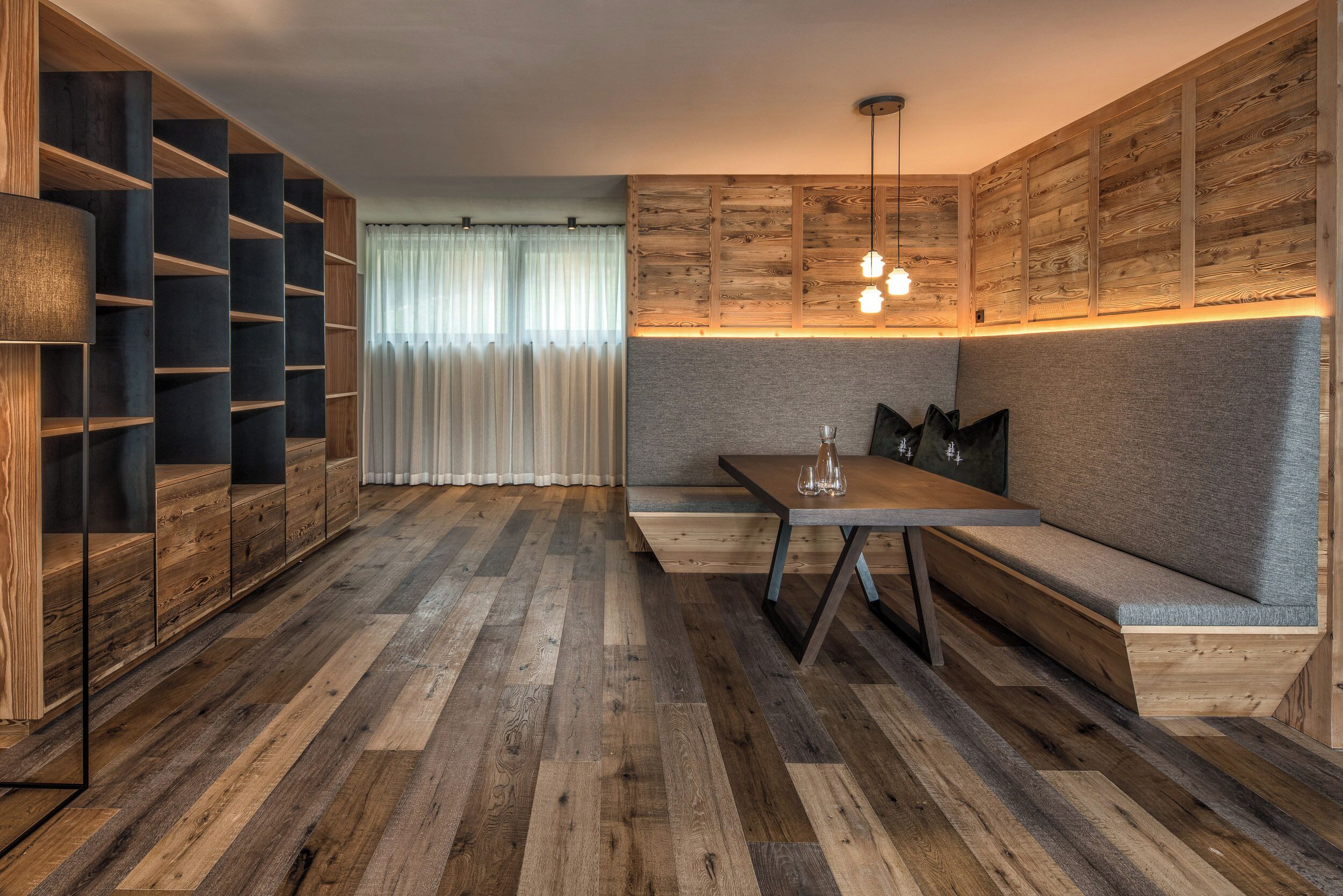 A modern interior with a wooden floor, built-in shelving, a cushioned bench, and a table with glasses.