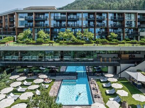 Un hotel moderno con piscina en la azotea, varios balcones y exuberante jardinería.