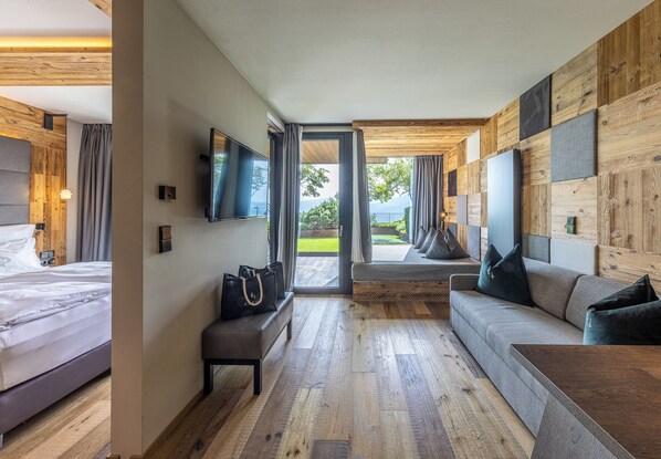 A modern hotel room with a wooden floor, a bed, a sofa, and a TV mounted on the wall.