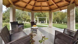 A covered patio area with wicker furniture and a grill, surrounded by a garden. - Beautiful home in Slime (Slime)