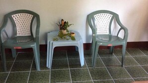 To grønne plaststole med hvide netrygge, et lille hvidt bord med en plante, og et fliset gulv.