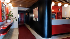 Un hall d’hôtel avec un tapis rouge, un comptoir d’accueil noir et un plafond en bois agrémenté de luminaires suspendus.