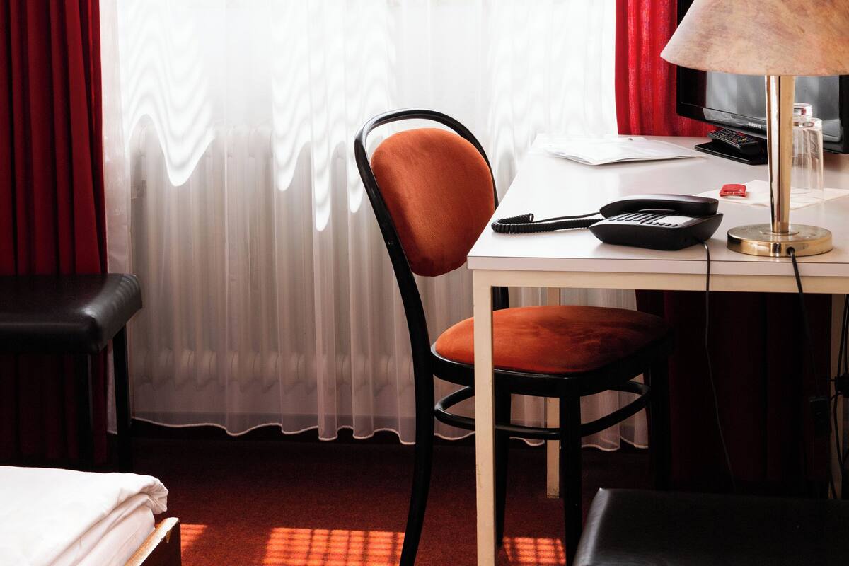 Ein Hotelzimmer mit einem Bett, einem Schreibtisch mit Lampe, einem Sessel und einem Fernseher.