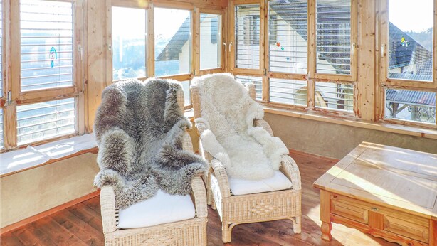 A room with two wicker chairs, one with a grey fur throw and the other with a white fur throw, and a wooden table. - Ferienhaus mit Pool und Sauna (Breitenfeld)