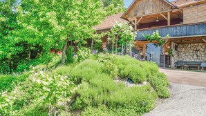 A rustic wooden building with a stone facade, a balcony with outdoor seating, and a lush garden with various plants and flowers. - Ferienhaus mit Pool und Sauna (Breitenfeld)
