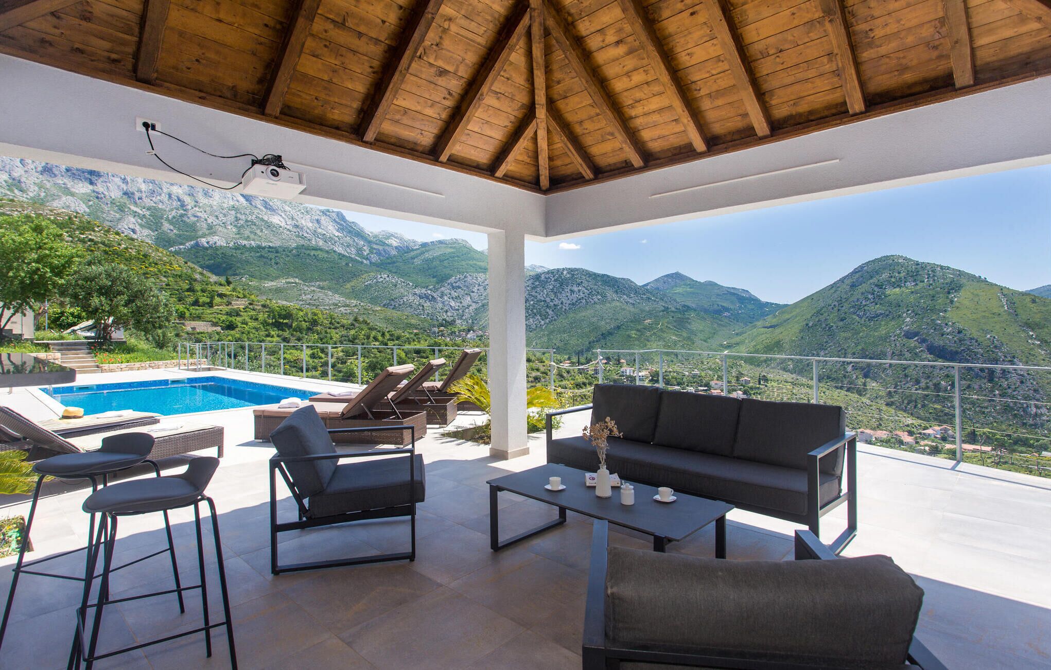 A covered outdoor seating area with a pool, lounge chairs, and a sofa.