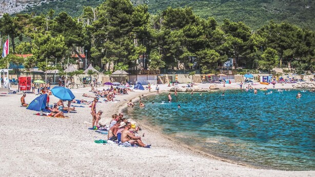 A beach with clear blue water, umbrellas, and people sunbathing. - Nice home in Zrnovnica (Zrnovnica)