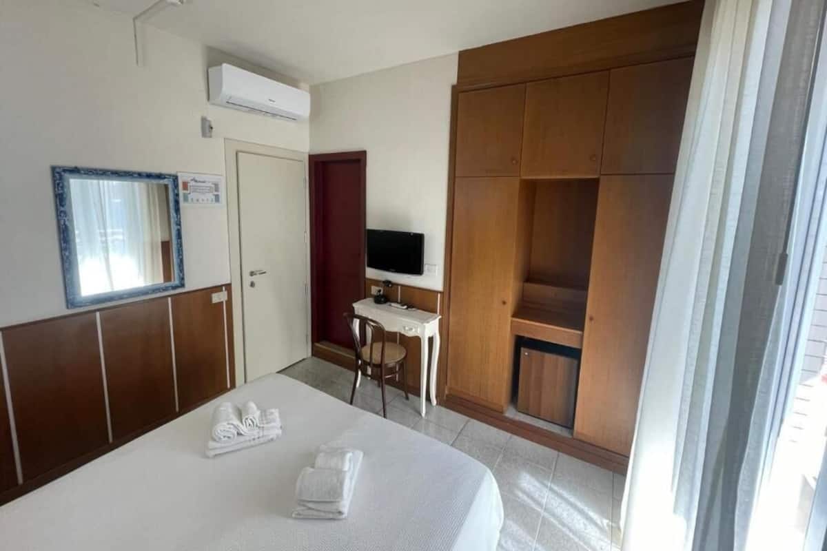 Una habitación de hotel con cama, escritorio, televisor y armario.