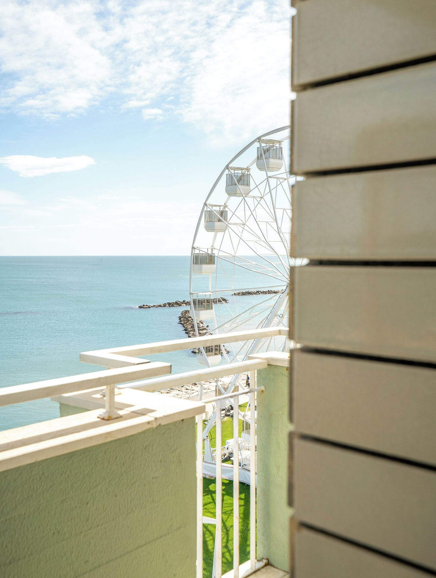 Un balcón con vistas a una noria y al mar.