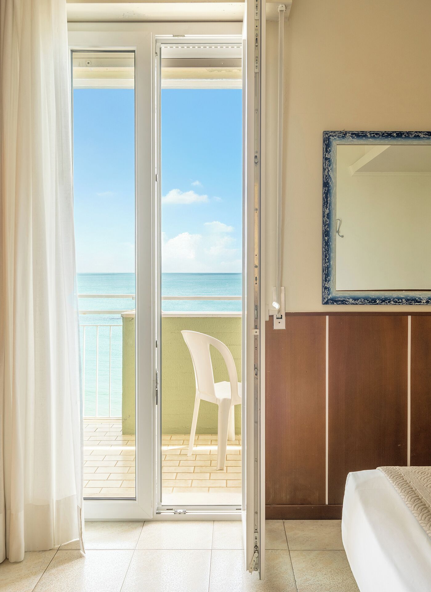 Habitación de hotel con puerta corrediza de vidrio que da a un balcón con vista al mar.