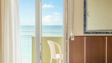 Habitación de hotel con puerta corrediza de vidrio que da a un balcón con vista al mar.