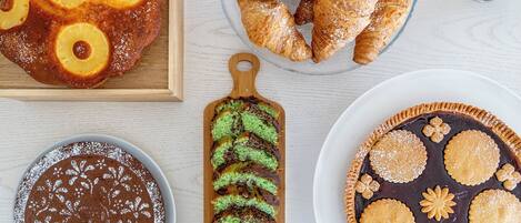 Variedad de postres, incluyendo pastel de piña, croissants, pastel de chocolate, pastel verde mármol y una tarta con galletas decorativas.