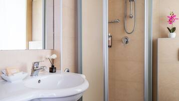 A bathroom with a white sink, a glass shower enclosure, and a potted orchid.