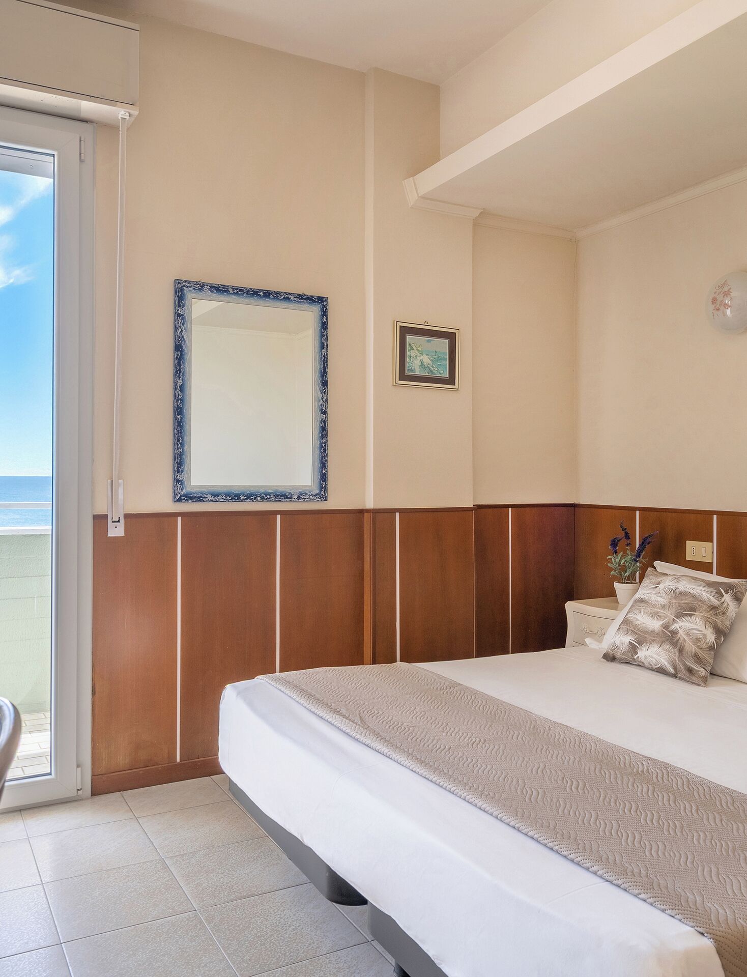 Une chambre d’hôtel avec un lit, une fenêtre, une porte et un tableau accroché au mur.