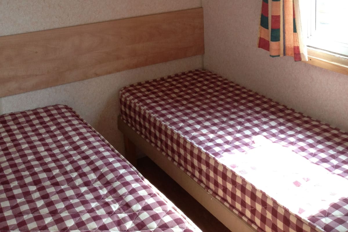 Een kleine, compacte kamer met twee eenpersoonsbedden, een raam met gordijnen en een houten hoofdbord.