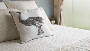 A neatly made bed with a textured white cover, a pillow with an ostrich design, and a small potted plant on the nightstand. - Camping la kilienne (Warlincourt-lès-Pas)