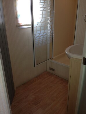 Een kleine badkamer met een houten vloer, een wit wastafelmeubel en een raam met een decoratief zonnescherm.