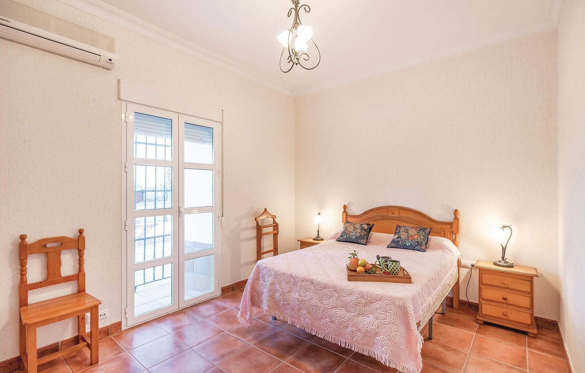 A bedroom with a bed, two bedside tables, a nightstand, a chair, a window, and a ceiling light.