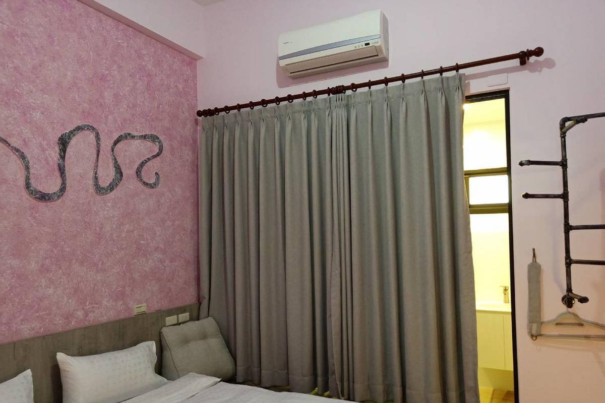 Una habitación de hotel con cama, cabecera, aire acondicionado de pared y cortina.