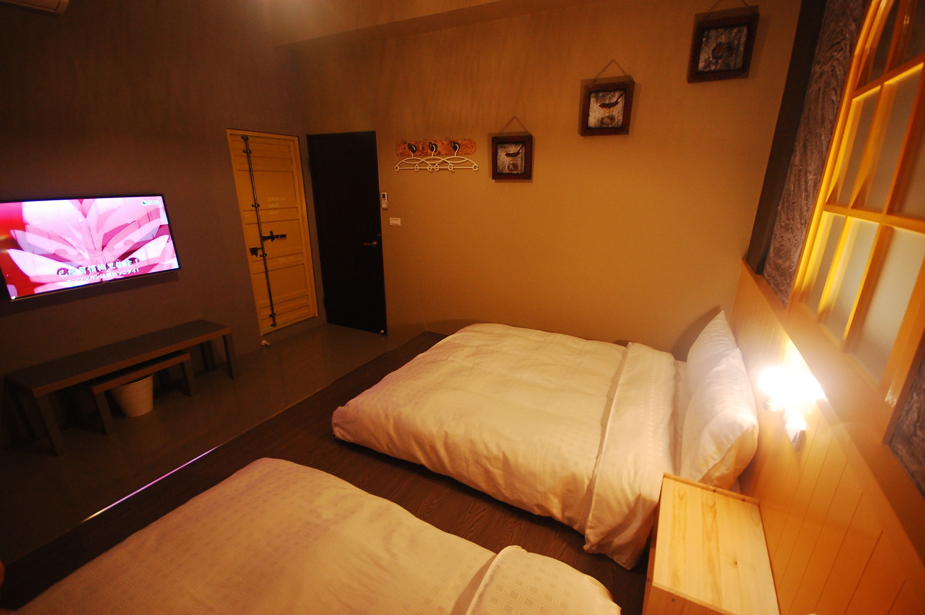 A hotel room with two beds, a TV on the wall, a bench, and a wooden door.