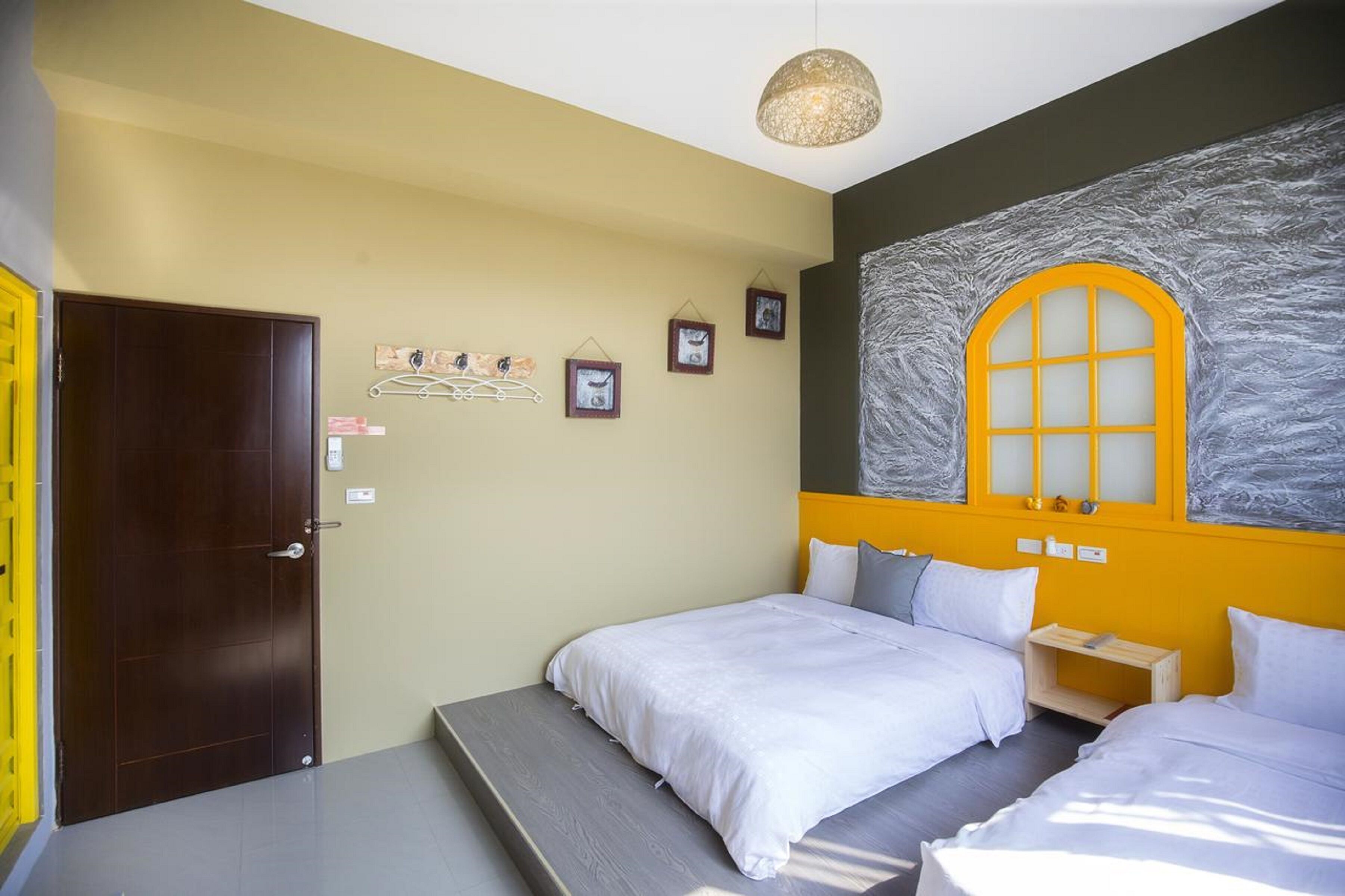 Habitación de hotel con dos camas, una mesita pequeña, un estante en la pared con fotografías y un ventanal con un diseño de vidrio esmerilado.
