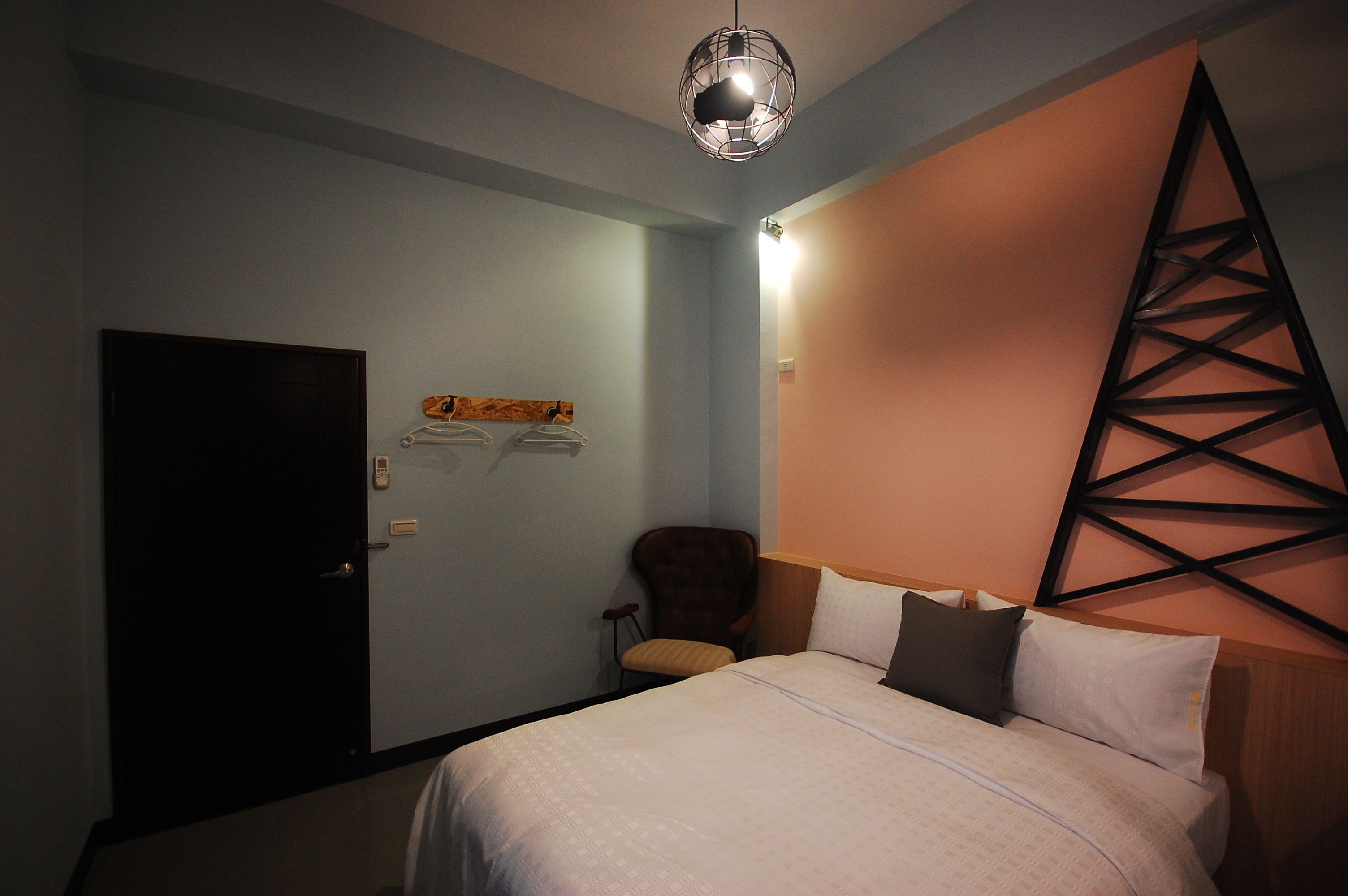 Una habitación de hotel con cama, una silla, perchero y puerta.