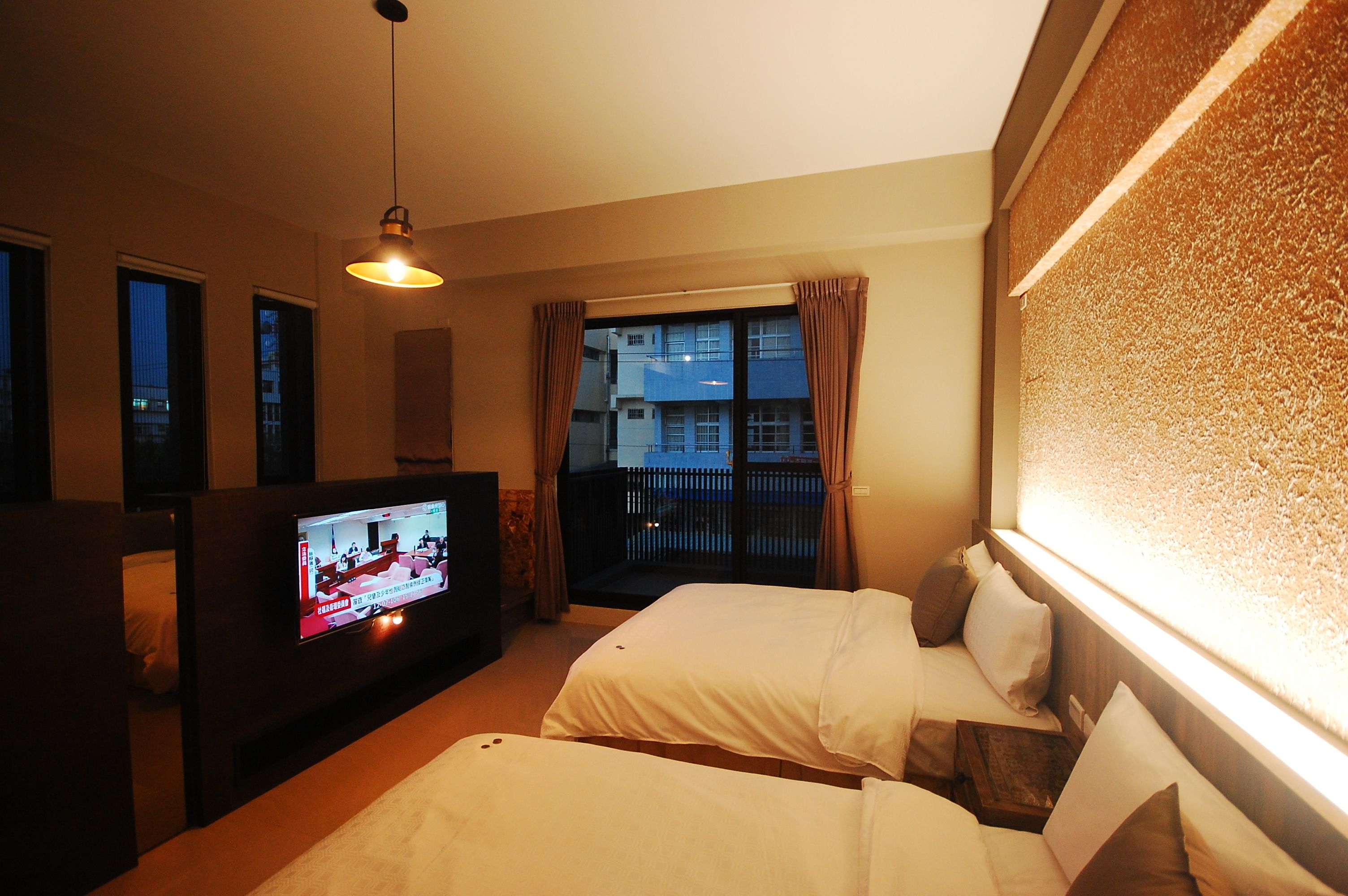 A hotel room with two beds, a TV, and a balcony with curtains.
