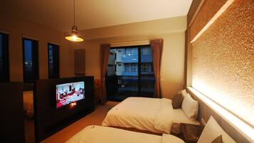 A hotel room with two beds, a TV, and a balcony with curtains.