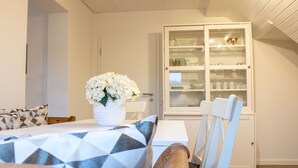 A dining area with a table set for two, a white cabinet with glass doors, and a window with a view. - Ferienhaus Domblick Herkenrath (Bergisch Gladbach)