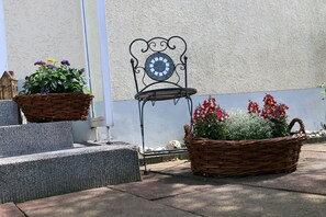 A metal chair with a clock, two wicker baskets with flowers, and steps leading to a door. - Ferienhaus Domblick Herkenrath (Bergisch Gladbach)