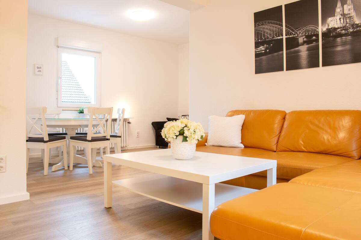 A modern living room with a white coffee table, an orange leather sofa, and a dining area with a white table and chairs.