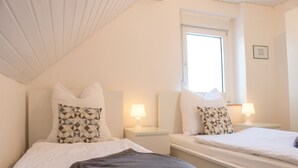 A twin room with two beds, each with a pillow, bedside tables with lamps, and a window. - Ferienhaus Domblick Herkenrath (Bergisch Gladbach)