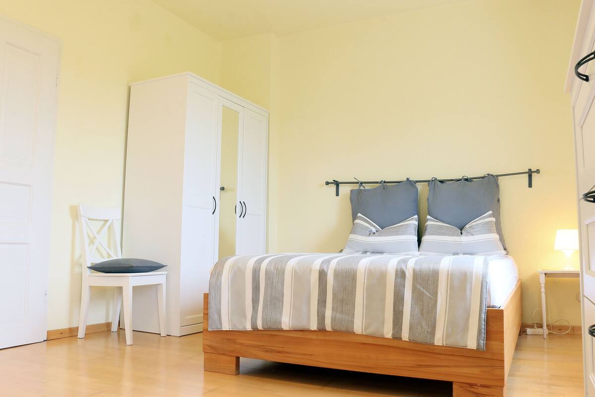 A bedroom with a bed, a chair, a wardrobe, and a bedside table with a lamp.