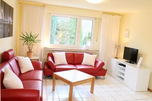 A living room with red sofas, a wooden coffee table, a TV on a white stand, and a window with curtains. - Ferienhaus Domblick Herkenrath (Bergisch Gladbach)