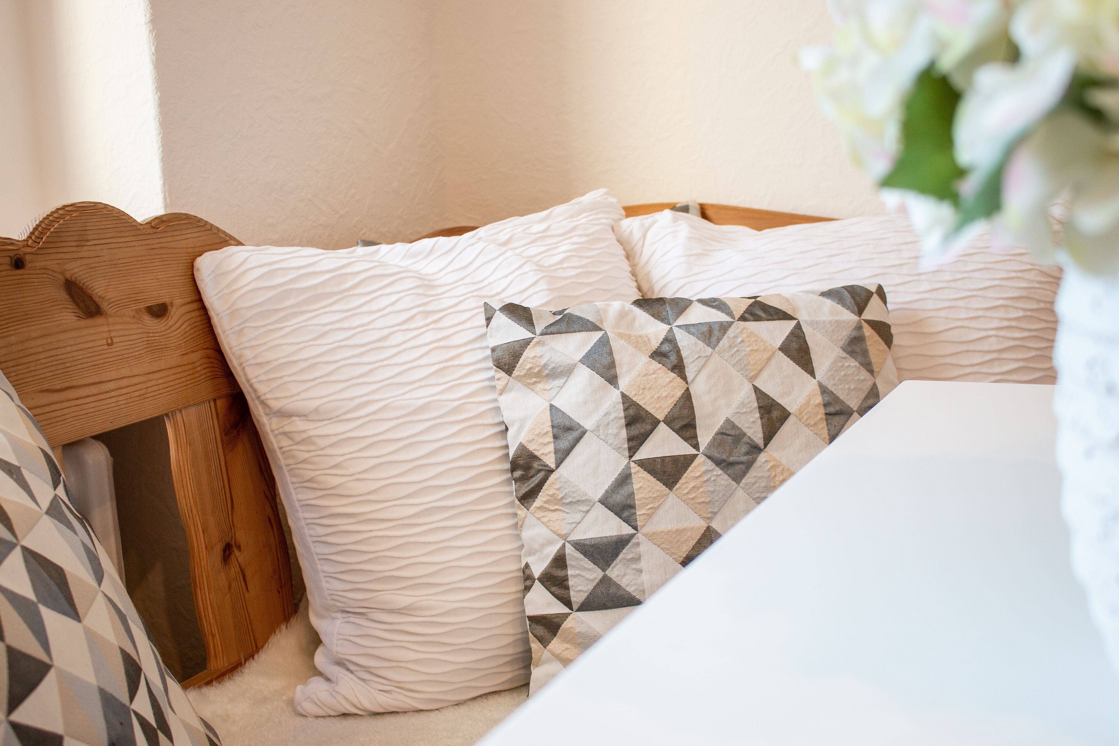 A bed with a wooden headboard, white and patterned pillows, and a white wall.