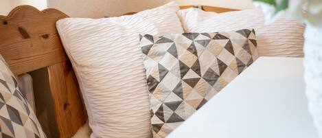 A bed with a wooden headboard, white and patterned pillows, and a white wall.