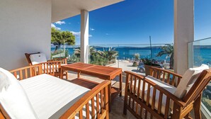 Een balkon met houten meubels, uitzicht op zee en een heldere lucht.