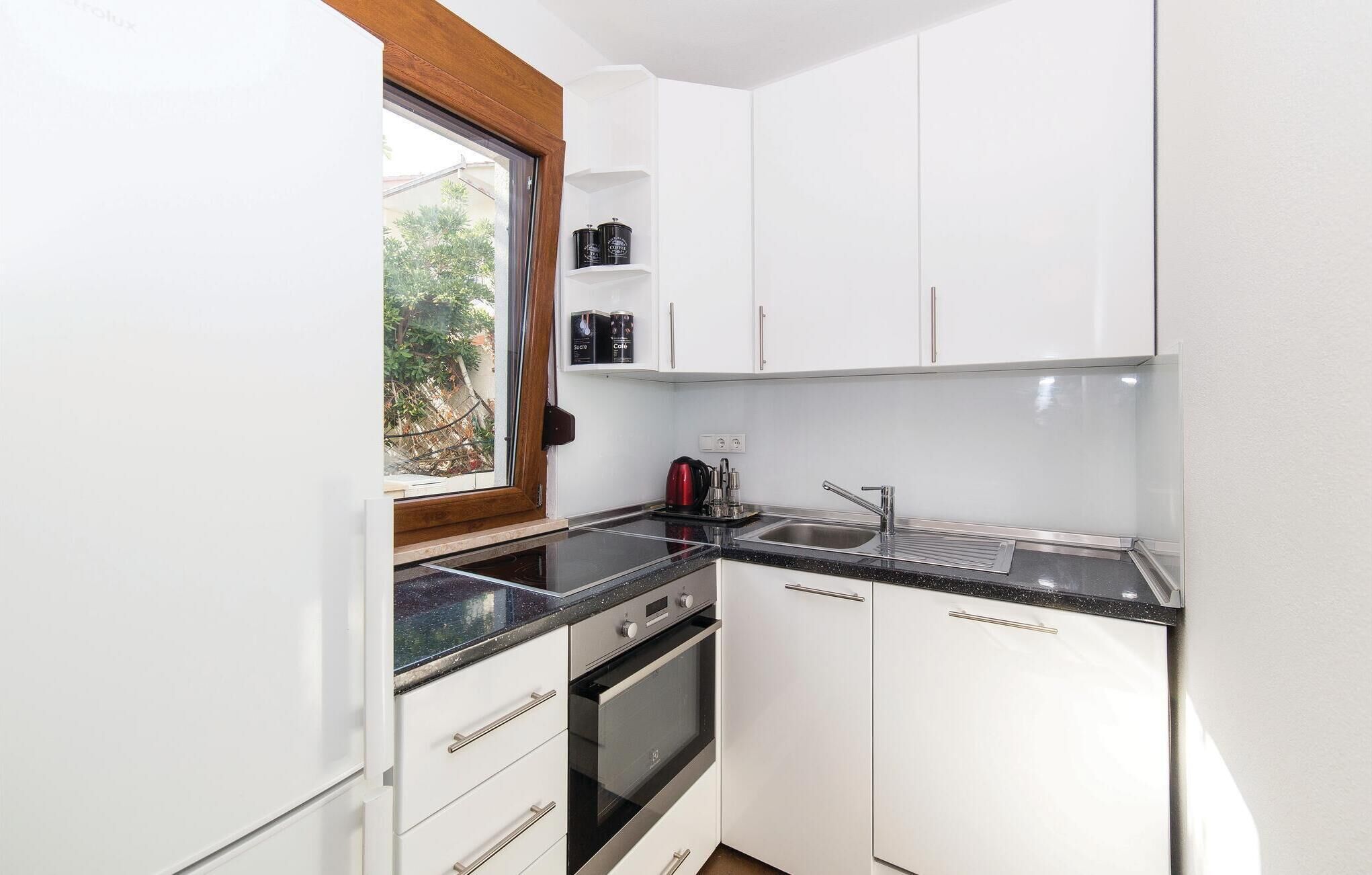 A compact kitchen with white cabinets, a black countertop, a window, and a built-in oven.