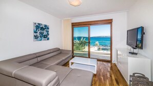 Een moderne woonkamer met een grijze bank, een flatscreen televisie en een groot raam met uitzicht op zee.