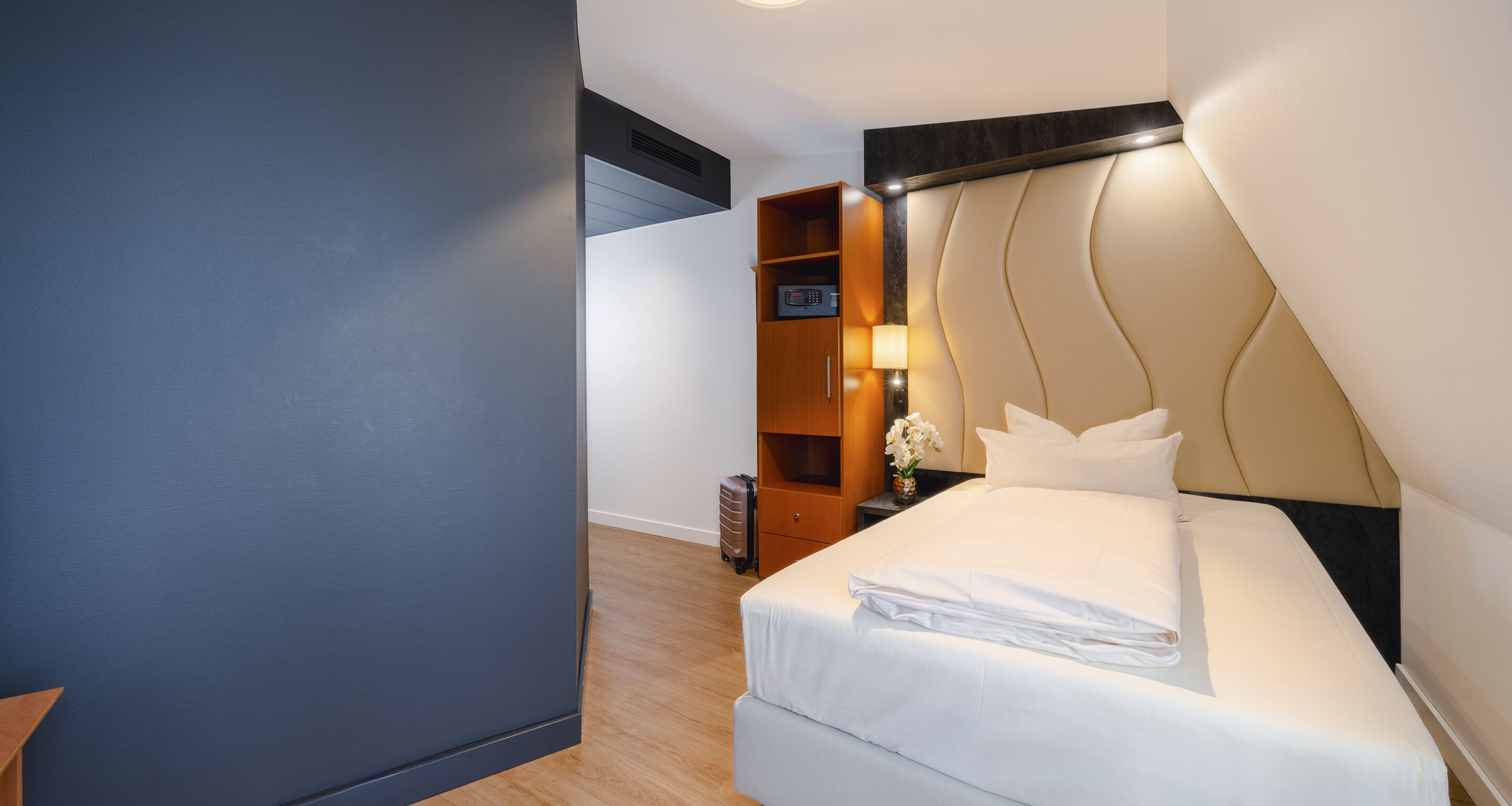 A hotel room with a bed, a nightstand, a lamp, and a wooden wardrobe.