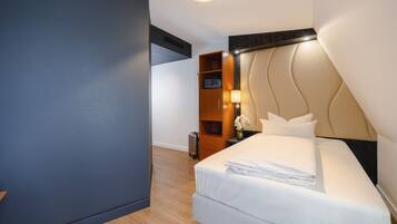 A hotel room with a bed, a nightstand, a lamp, and a wooden wardrobe.
