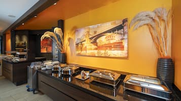 Un buffet composé de différents plats présentés dans des récipients, un grand tableau représentant un pont et des décorations à base de plumes d’herbe des pampas.