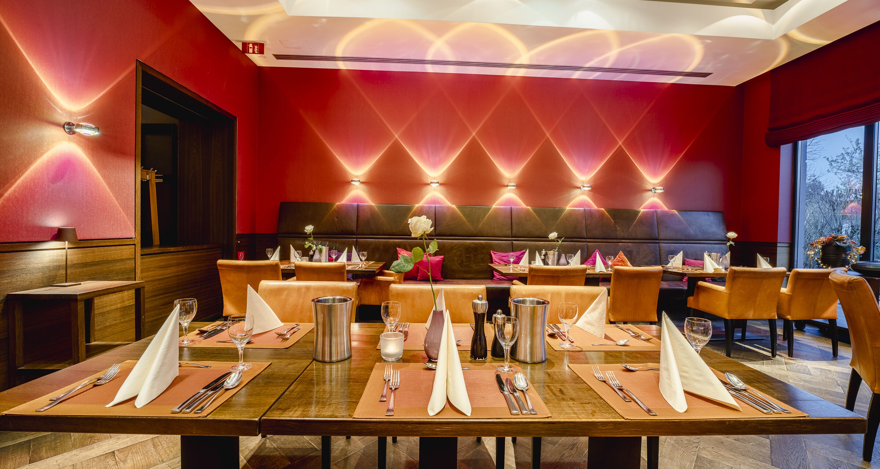 A restaurant with a red wall, a long table set for dining, and a modern ceiling design.