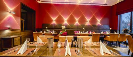 A restaurant with a red wall, a long table set for dining, and a modern ceiling design.