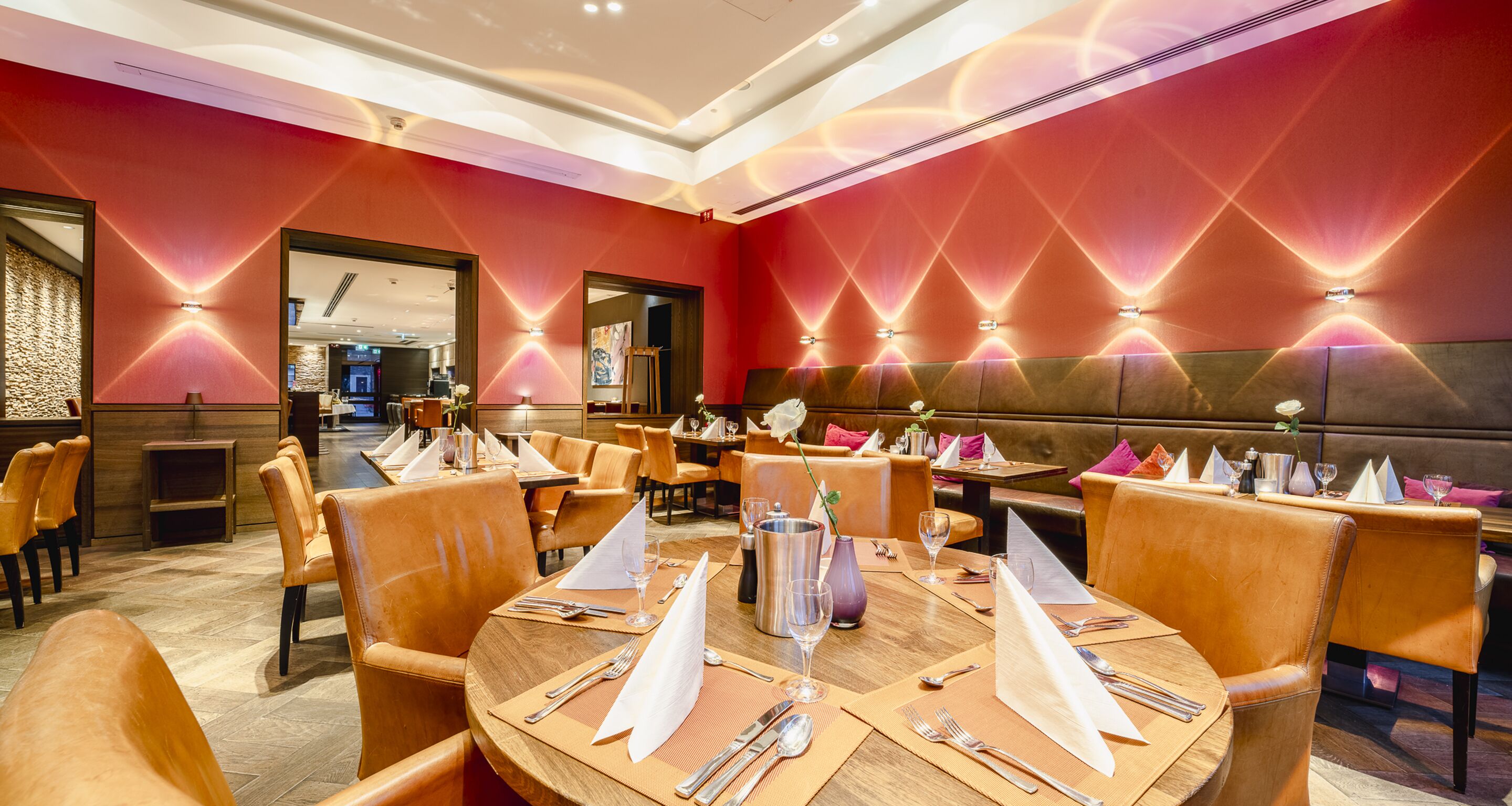 Een restaurant met ronde tafels, oranje stoelen en rode muren.