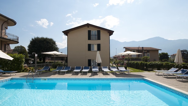 Une piscine entourée de bâtiments et de montagnes, avec des chaises longues et des parasols.