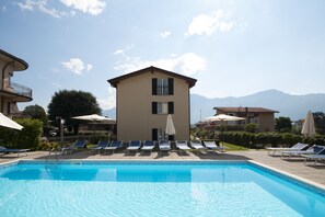Une piscine entourée de bâtiments et de montagnes, avec des chaises longues et des parasols.