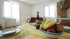 Une table à manger avec une bouteille de vin, un saladier de fruits et des verres à vin vides.