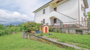 Ein zweistöckiges Haus mit roter Tür, einer kleinen Veranda und einer Steinmauer davor.